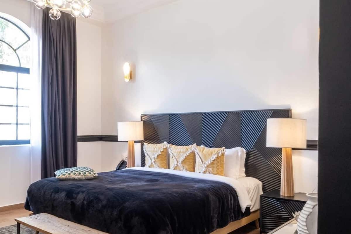 A modern bedroom with a large bed, bedside lamps, a bench, and a decorative sculpture.