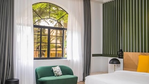A bedroom with a large window, a green sofa, a wooden bedside table, and a bed with a white duvet. - Le Palais d'Akwa (Abidjan)