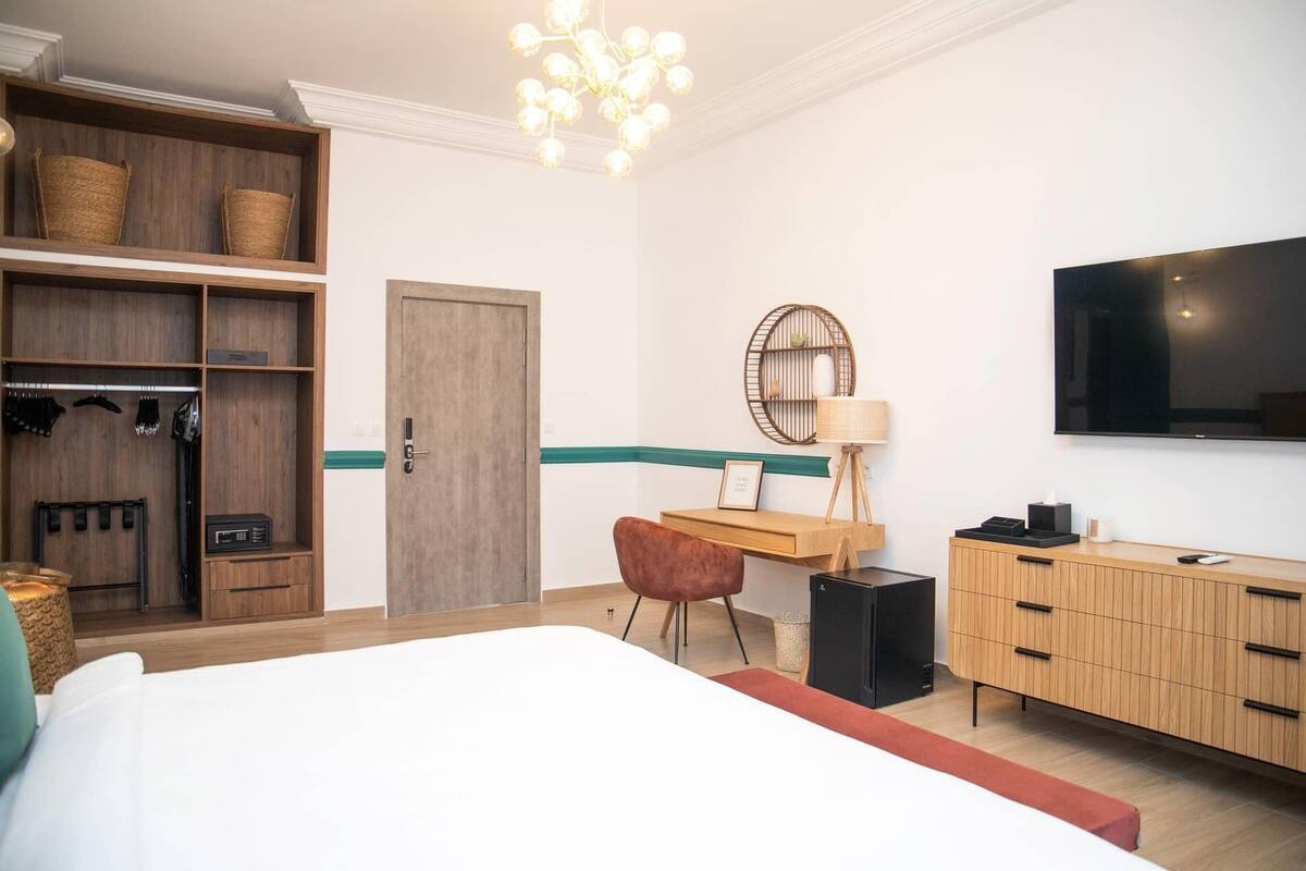 A hotel room with a bed, a desk, a wardrobe, a television, and a chandelier.