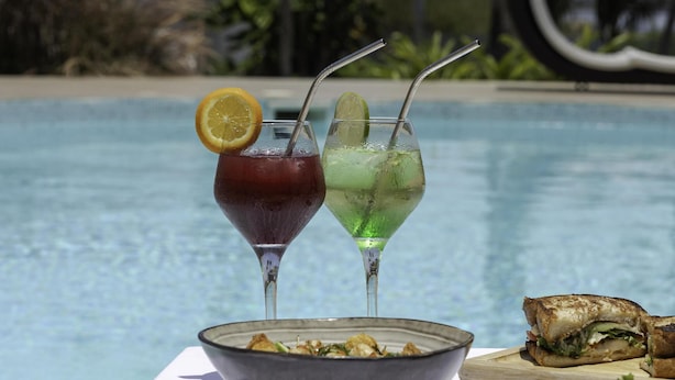 A table with two drinks, a bowl of food, and a sandwich by a poolside. - Le Palais d'Akwa (Abidjan)