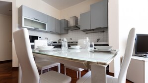 A modern kitchen with white cabinetry, a glass dining table, and white chairs. - Italianway Easy - Sismondi 74 (Milan)