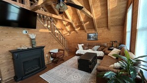 Un acogedor interior de cabaña de madera con chimenea, un sofá, una mesita de centro y una escalera.