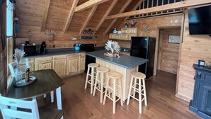 Una cocina amplia con vigas de madera, una isla central con taburetes, una mesa de comedor y un televisor montado en la pared.