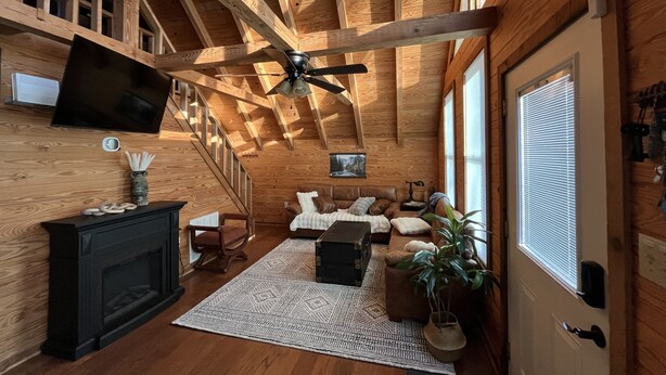 Un interior acogedor de madera con techo abovedado, una chimenea, un espacio de estar confortable y un televisor montado en la pared.
