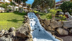 A water slide in a resort area with palm trees and a building in the background. - Ocean View Apartment in Golf del Sur (Golf del Sur)