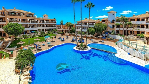A resort with a central swimming pool, multiple balconies, and palm trees. - Ocean View Apartment in Golf del Sur (Golf del Sur)