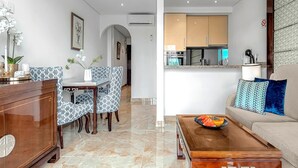 A modern living room with a wooden coffee table, patterned chairs, a sofa with cushions, and a kitchen area in the background. - Ocean View Apartment in Golf del Sur (Golf del Sur)