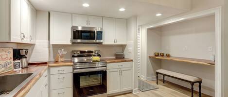 A modern kitchen with white cabinetry, stainless steel appliances, and a wooden countertop.
