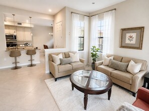 A living room with a sofa, a coffee table, and a kitchen in the background.