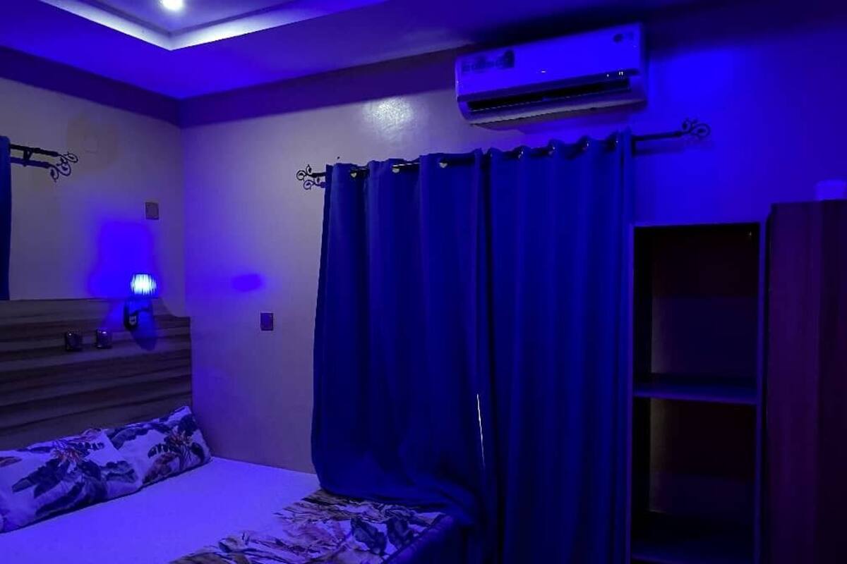 Une chambre à coucher comprenant un lit, des rideaux, un appareil de climatisation et une étagère fixée au mur.