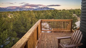A wooden deck with a chair, overlooking a forested area with mountains in the background.