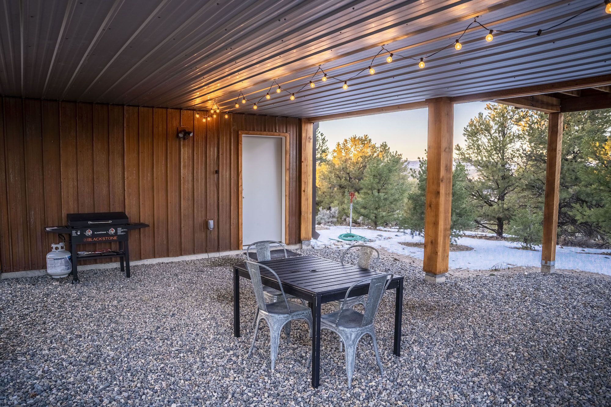 Une terrasse extérieure avec un barbecue, une table et des chaises, entourée de gravier et de murs en bois.