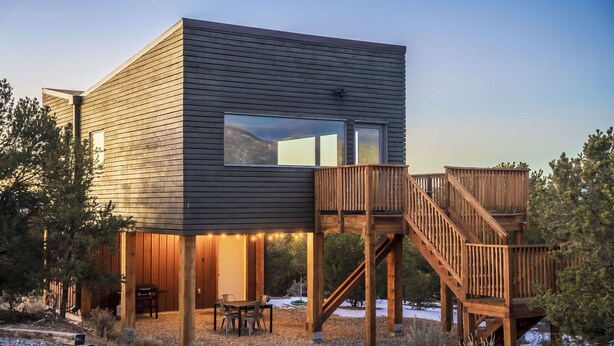 A modern cabin with a wooden deck and a staircase leading to a second level.