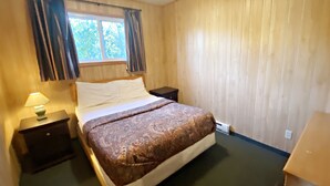 Un dormitorio con cama, mesita de noche, lámpara y ventana con cortinas.