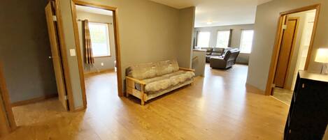 Een ruime woonkamer met houten vloeren, een bank en een eethoek met tafel en stoelen.