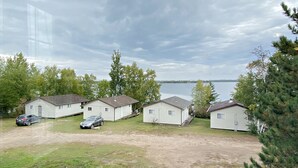 A row of single-story mobile homes with a lake view, a dirt driveway, and a parked car.