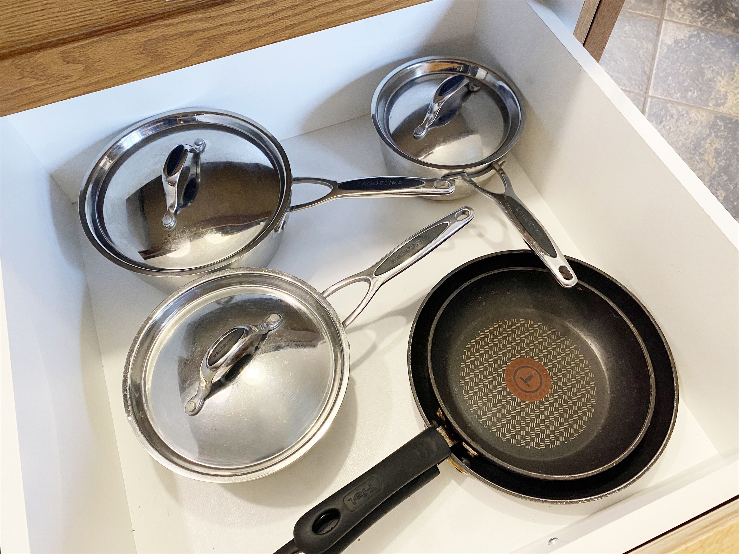 A kitchen counter with three stainless steel pots and a black frying pan.