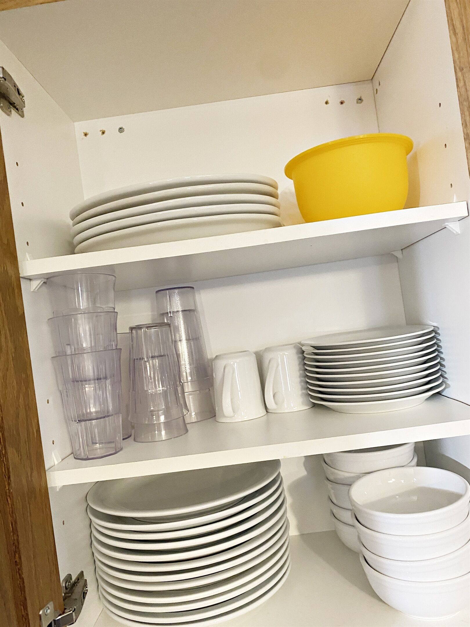 Une étagère blanche sur laquelle sont empilées des assiettes blanches, un bol jaune et des gobelets en plastique transparent.
