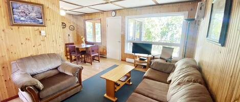A cozy living room with a wooden interior, a sofa set, a dining table, and a television.