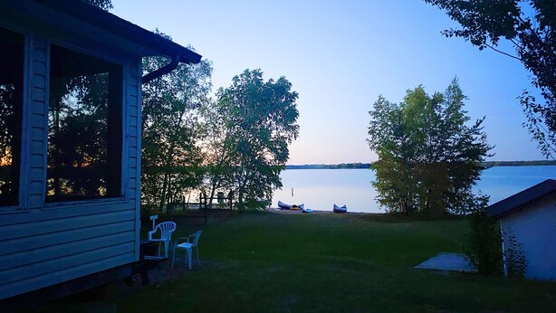En hytte ved søen med en terrasse, stole og kanoer ved vandet.