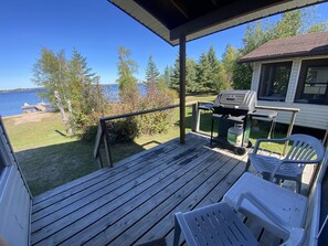 Une terrasse en bois avec un barbecue, des chaises et une vue sur un lac et des arbres.