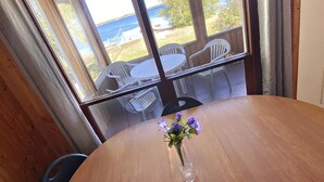 A wooden dining table with a clear vase of flowers, a view of a beach and chairs outside. - "Lakeside Landing" Escape to paradise (Seven Sister Falls)