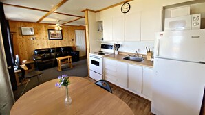 A compact kitchen with white appliances, a dining table with a vase of flowers, and a black leather sofa in the living area. - "Lakeside Landing" Escape to paradise (Seven Sister Falls)