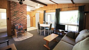 A living room with a brick wall, a dining table with chairs, a sofa, a TV, and a fireplace.