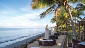 A beachside restaurant with outdoor seating, palm trees, and a view of the ocean. - Fiji -Whyndham- Beachfront Resort- Denarau - 3 BR (Denarau Island)
