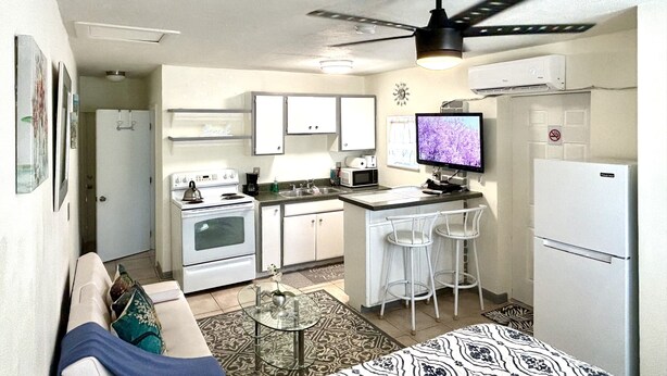 Un espacio habitable compacto con kitchenette, ventilador de techo, televisor de pantalla plana y sofá.
