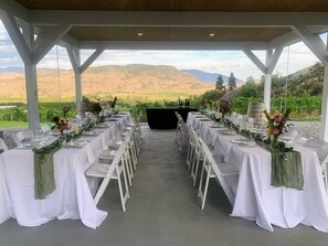 An outdoor covered dining area with tables set for a meal, overlooking a scenic landscape. - Oliver Oasis, Cab Franc: swim spa and 5 bdrm in the heart of wine country! (Osoyoos)