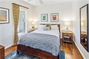 A bedroom with a bed, two bedside tables, a window with curtains, and two framed pictures on the wall.