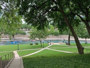 A park with a walking path, benches, and a river with boats. - Comal River Condo 323 | Comal Riverfront | Remodeled (New Braunfels)