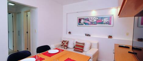 A dining area with a table set for two, a white sofa, and a painting on the wall.