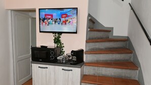A kitchen area with a microwave, toaster, and coffee maker on a countertop. A television is mounted on the wall above the counter.