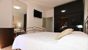 A bedroom with a bed, a TV mounted on the wall, a wardrobe, and a mirror.