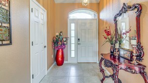 Un pasillo con una puerta blanca, un jarrón rojo con flores y un espejo sobre una consola de madera.
