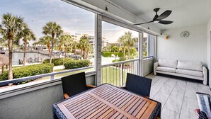 A balcony with a table and chairs, a sofa, a ceiling fan, and a view of a marina with palm trees. - Waterfront Marco Island Condo < 1/4 Mi to Beach! (Marco Island)