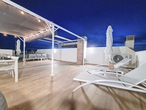 Relax and socialize on this rooftop terrace with lounge chairs and a dining table for two, featuring climate control and a shaded area under a pergola.