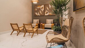 A modern living room with a sofa, two wicker chairs, a coffee table, and a large potted plant. - Wyndham Garden Mazatlan Marina (Mazatlán)