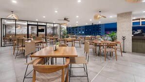 A spacious indoor dining area with wooden tables and chairs, ceiling fans, and large windows offering a view of the cityscape. - Wyndham Garden Mazatlan Marina (Mazatlán)