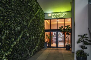 Entrada de un edificio moderno con un muro verde y un cartel que dice 'Wyndham Garden'.