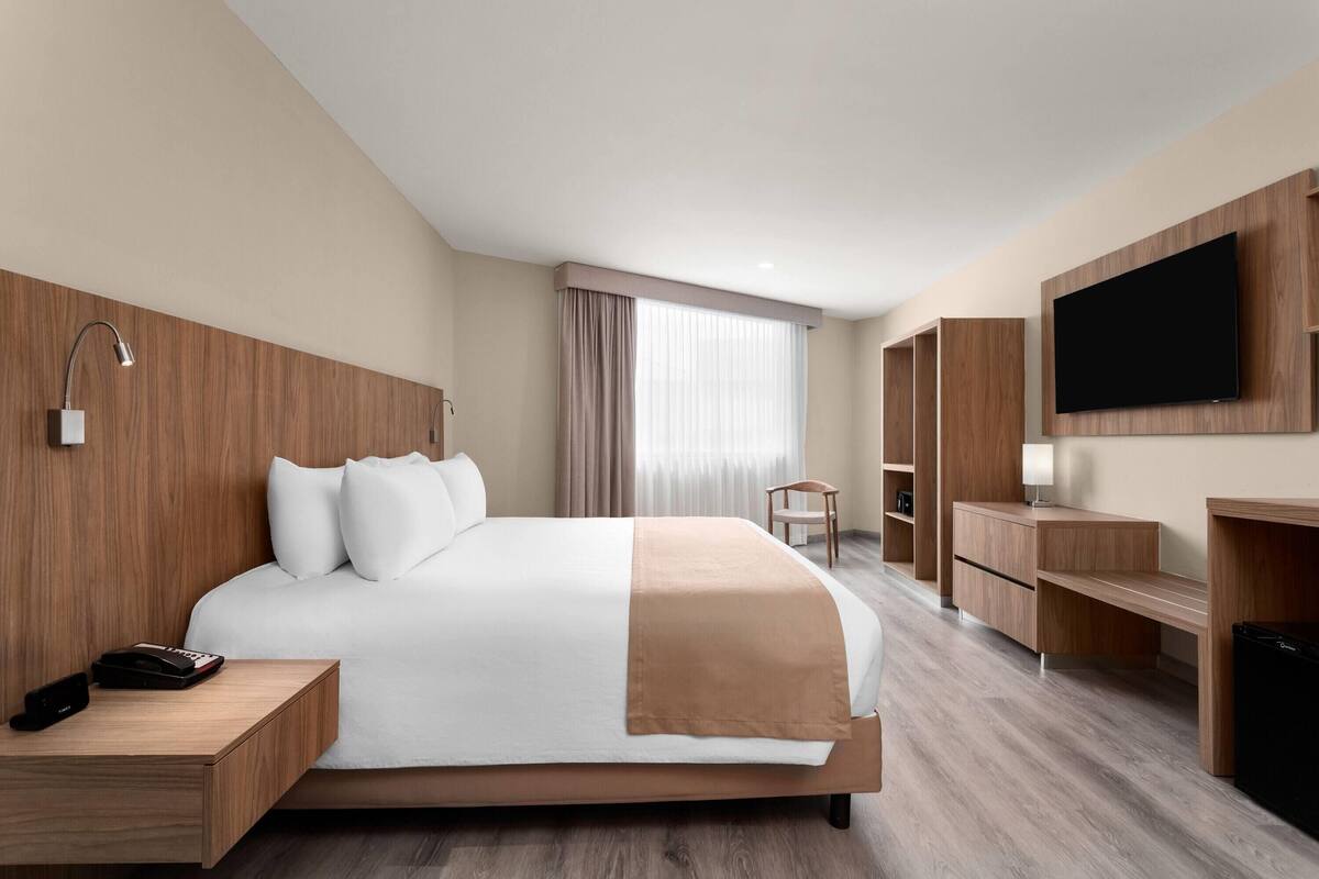 A modern hotel room with a large bed, wooden headboard, a flat-screen TV, a desk, and a chair.