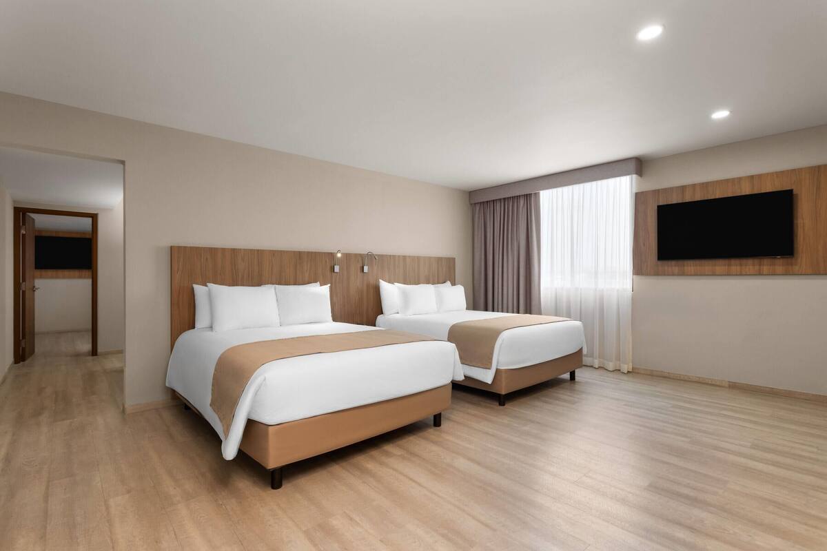 A hotel room with two beds, a flat-screen TV mounted on the wall, and a wooden floor.