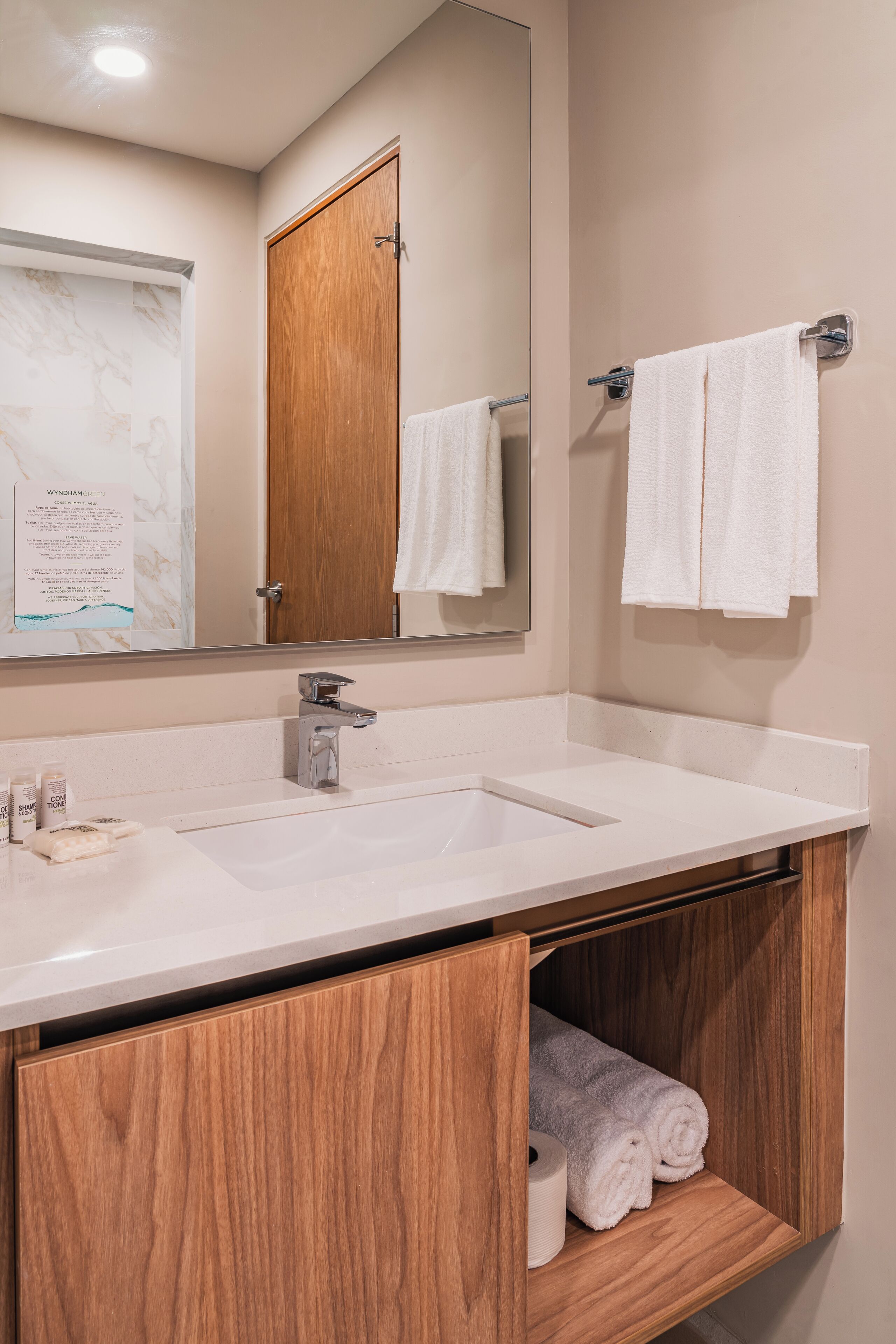 A bathroom with a wooden vanity, a large mirror, and two white towels hanging on hooks.