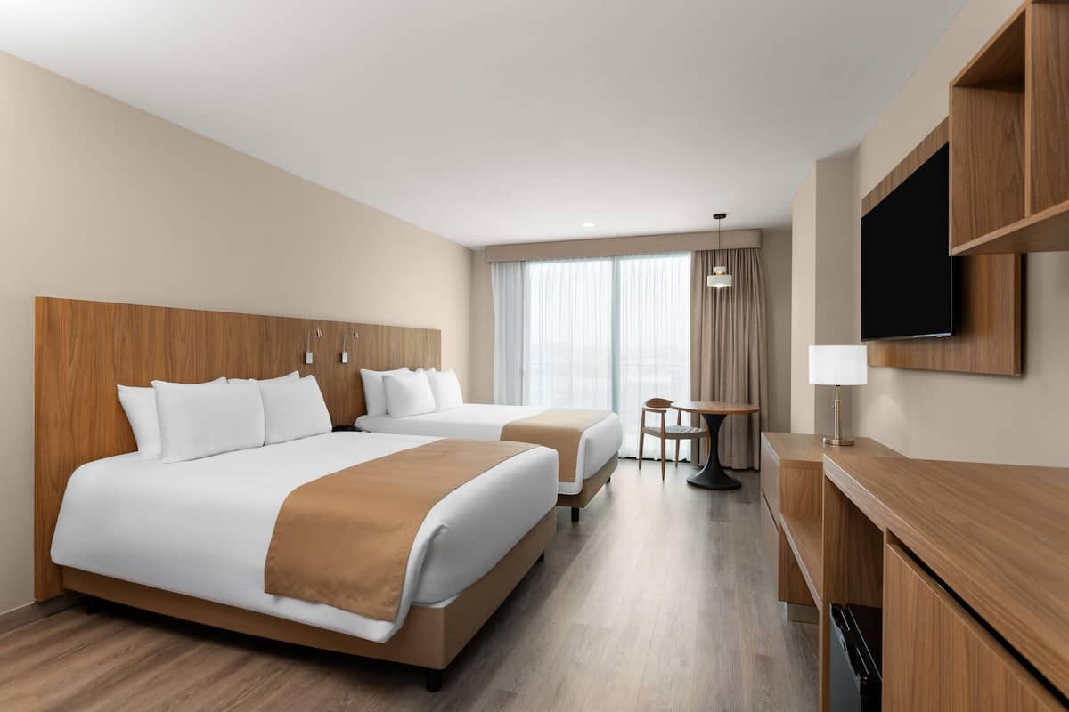 A hotel room with two beds, a desk, a TV, and a window with curtains.