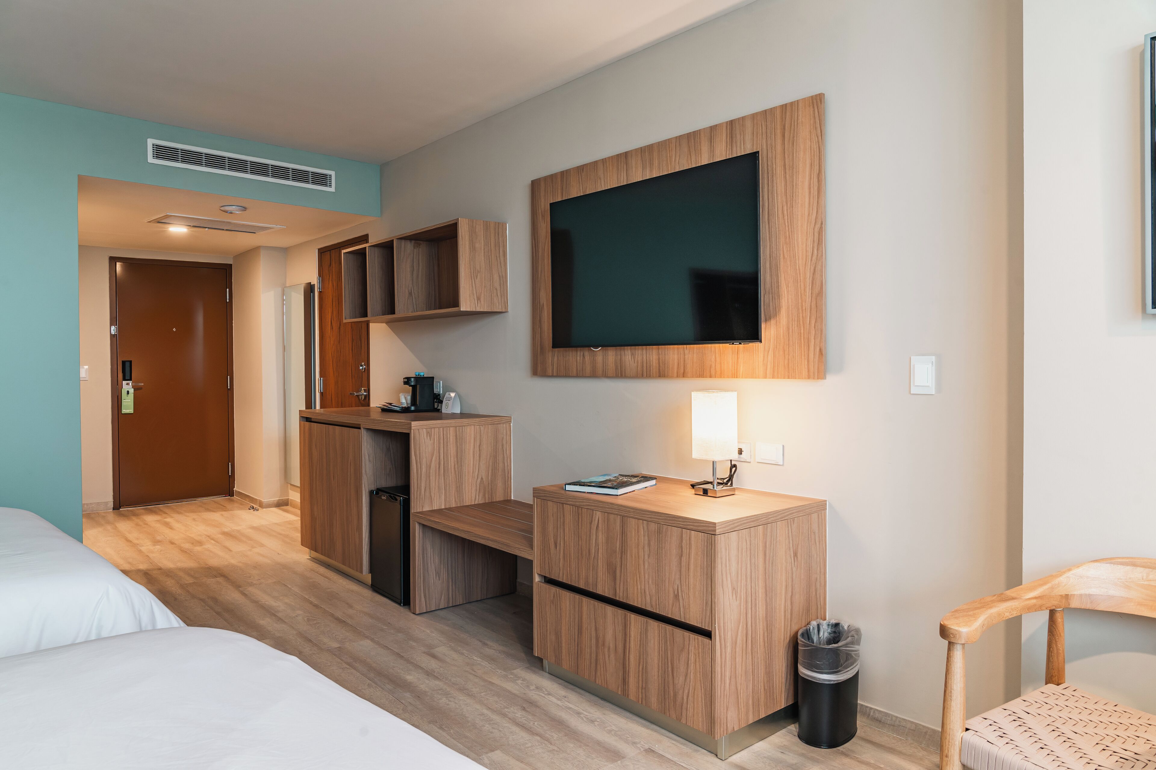 Habitación de hotel con cama, escritorio con lámpara, televisión y cubo de basura.