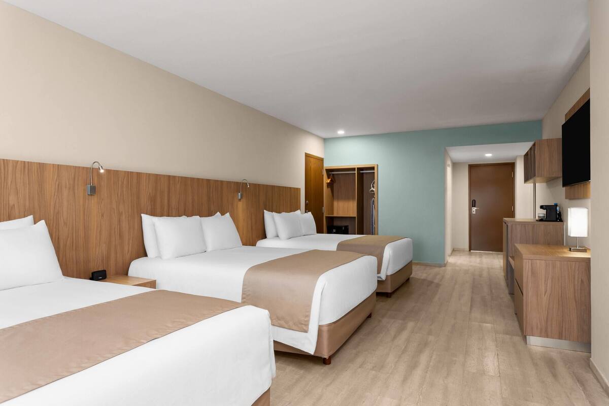 A hotel room with three beds, a wooden headboard, a TV, a desk, and a wardrobe.
