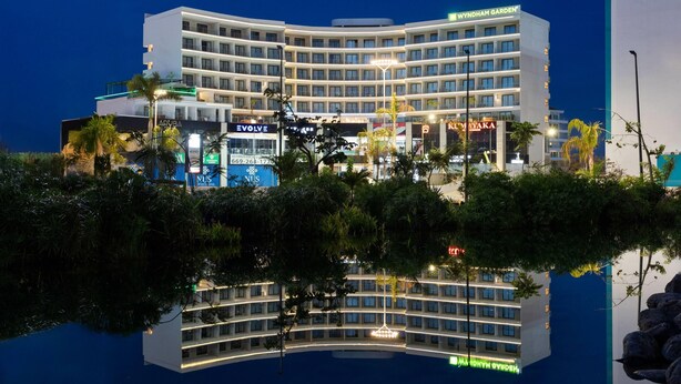 A modern hotel with a curved facade, multiple floors, and a reflection in the water. - Wyndham Garden Mazatlan Marina (Mazatlán)