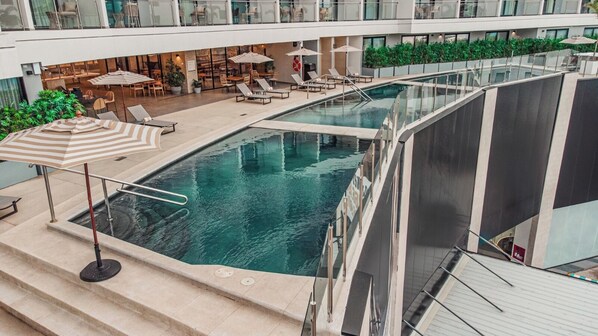 Una piscina en la azotea con barandilla de cristal, sillas de descanso y sombrillas.